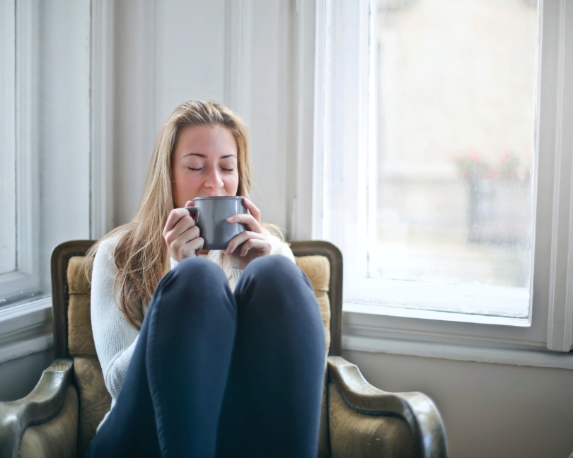Una donna sta bevendo una tisana calda seduta sulla poltrona di casa