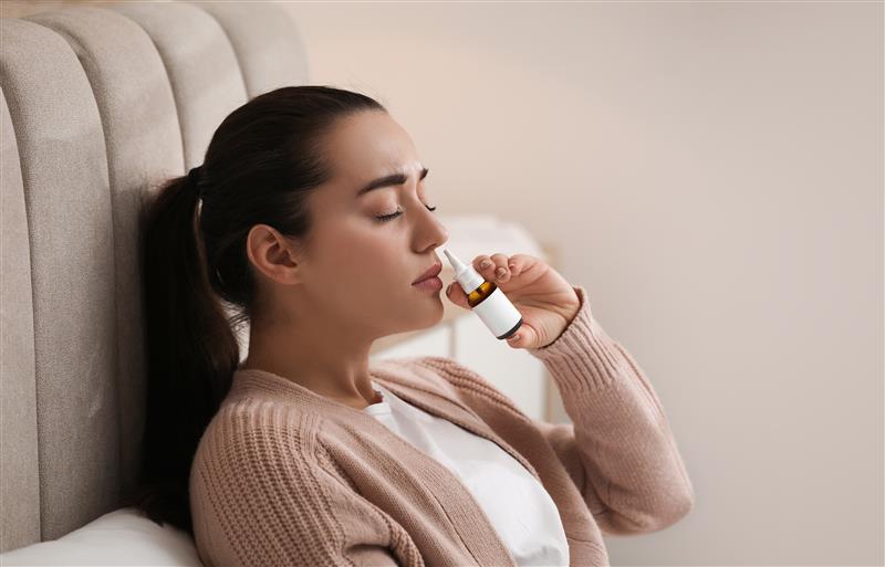 Una donna si sta spruzzando uno spray nasale seduta sul divano di casa