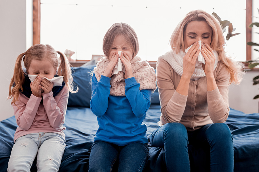 Mamma e due bambine sorridenti, si soffiano il naso sedute sul divano